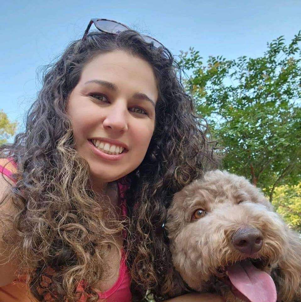 Woman with curly hair holding a dog outdoors with trees in the background