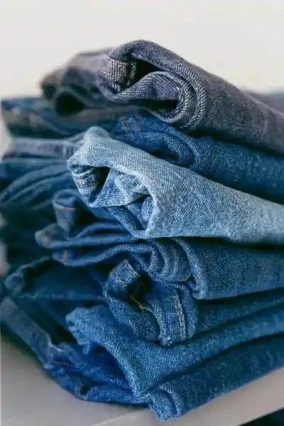 Stack of folded blue jeans on a white surface