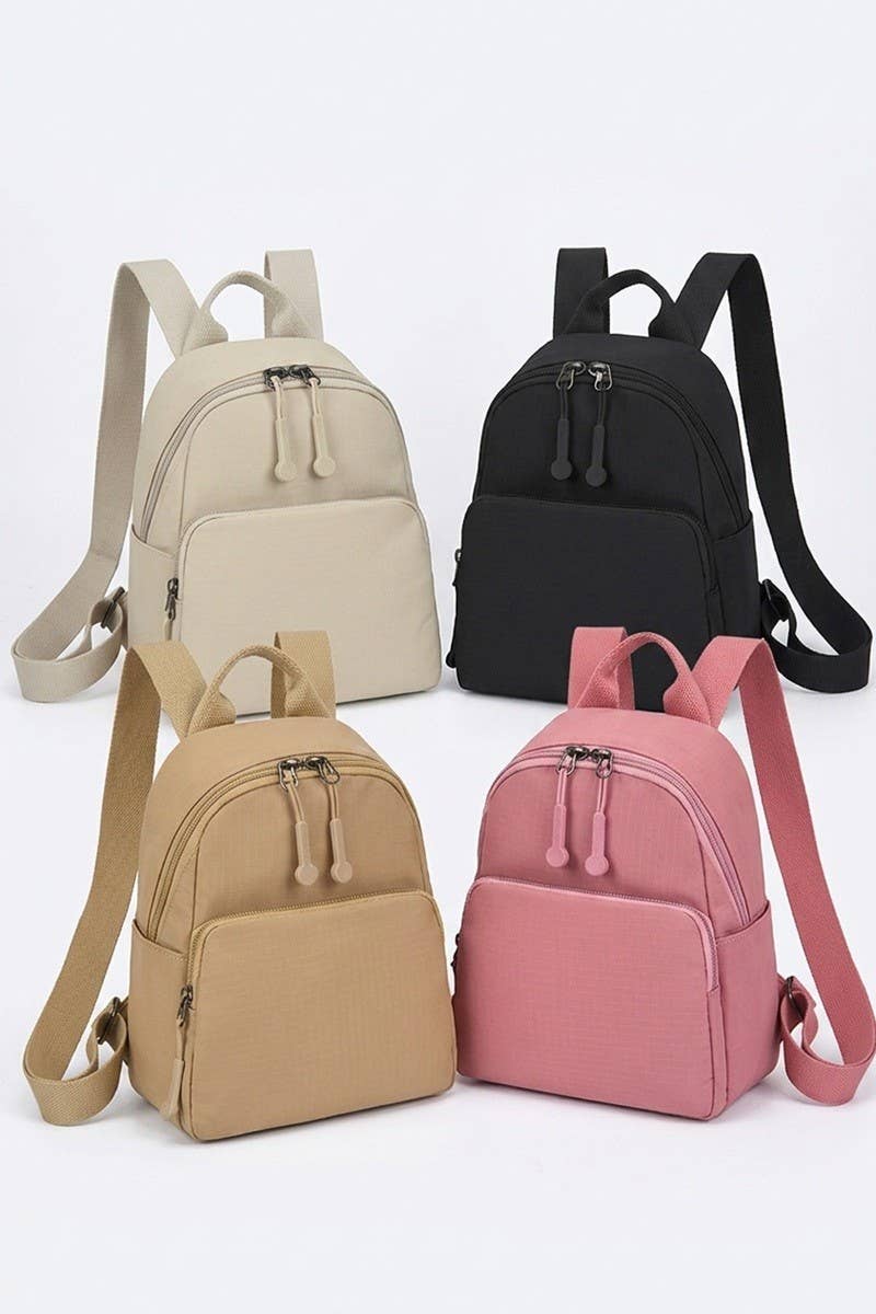 Four small backpacks in different colors are arranged on a light gray background: one cream, one black, one tan, and one pink. Each backpack has a zippered front pocket, top handle, and shoulder straps.